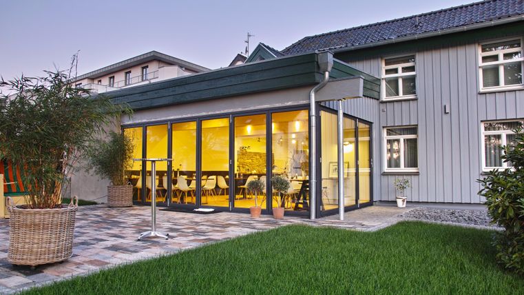 A modern extension with large windows and a cozy interior. The garden is well-kept with green grass and plants.