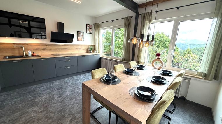Een moderne keuken met een eettafel en stijlvolle stoelen. Grote ramen bieden uitzicht op het groene landschap buiten.