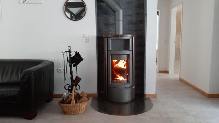 Een moderne haard staat in een lichte, gezellige ruimte. De ruimte heeft een ontspannende sfeer met een comfortabele bank en een wickerstandaard.