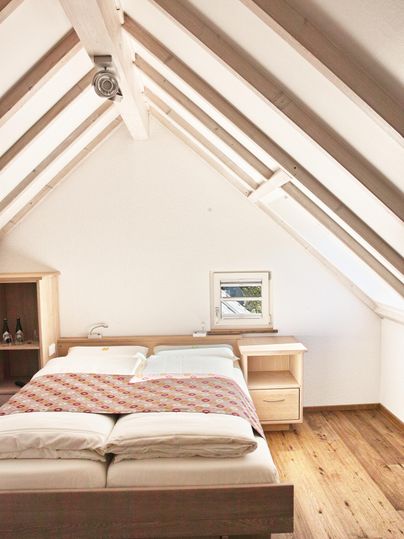 A cozy bedroom with a large bed and wooden flooring. The ceiling features a modern roof structure with exposed beams.