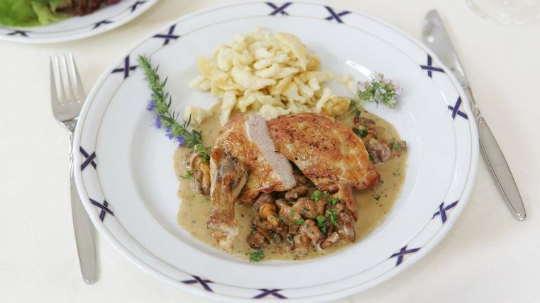 A delicious dish with fried chicken, mushrooms, and a creamy sauce. It is served with fresh spaetzle and some green herbs.
