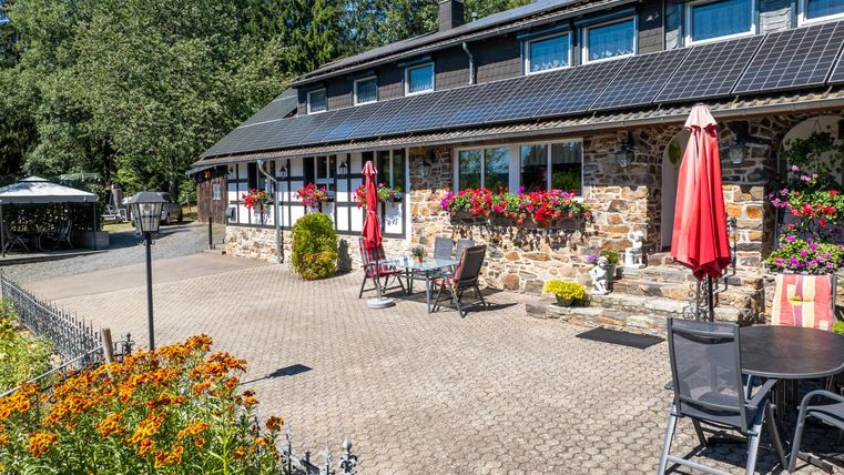 Een charmant huis met een stenen gevel en veel kleurrijke bloemen. Ruimte met zitgelegenheden en parasols in de buitenlucht.