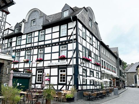 Een historisch vakwerkhuis met bloeiende bloembakken. Voor het gebouw zijn gezellige terrassen met tafels en stoelen.