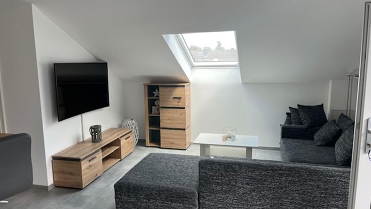 Een moderne woonkamer met een gezellige bank en een grote televisie. De kamer heeft lichte muren en veel natuurlijk licht door het dakraam.