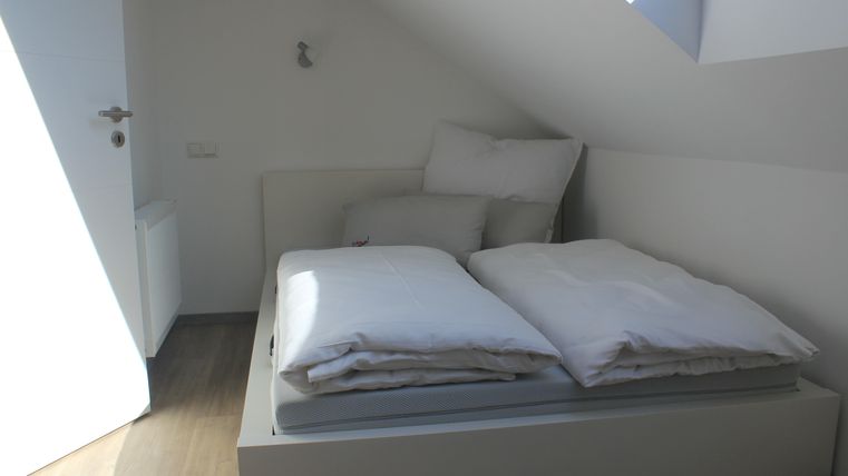 A bright bedroom with a white bed and two pillows. The room has a cozy atmosphere and skylights that let in daylight.