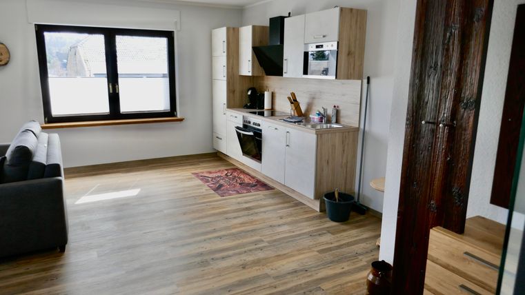A modern apartment with an open kitchen and a cozy sofa. The room has bright walls and a beautiful wooden floor.