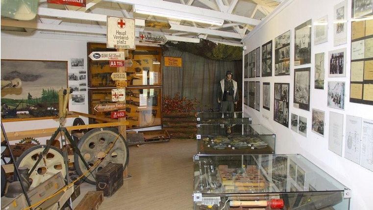 A museum with historical artifacts, including tools and photographs on the walls. In the center stands a statue, surrounded by display cases with various exhibits.