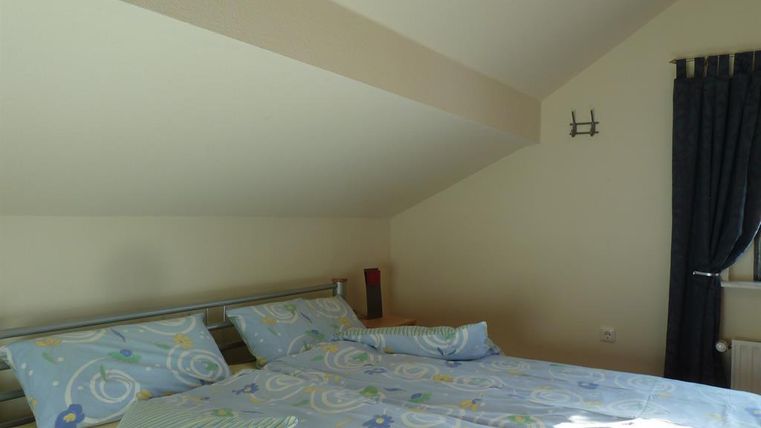 A bedroom with a double bed and blue bed linen. The room has a sloping ceiling and a window with curtains.