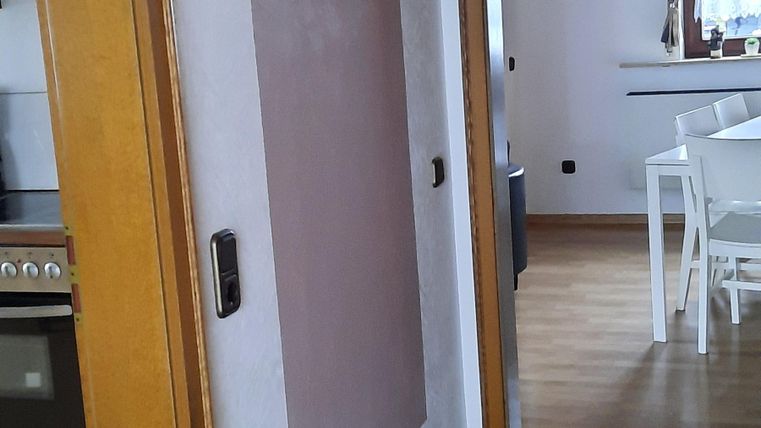 A bright interior with a hallway and wooden doors. Coat hooks hang on the wall, and the floor is carpeted.