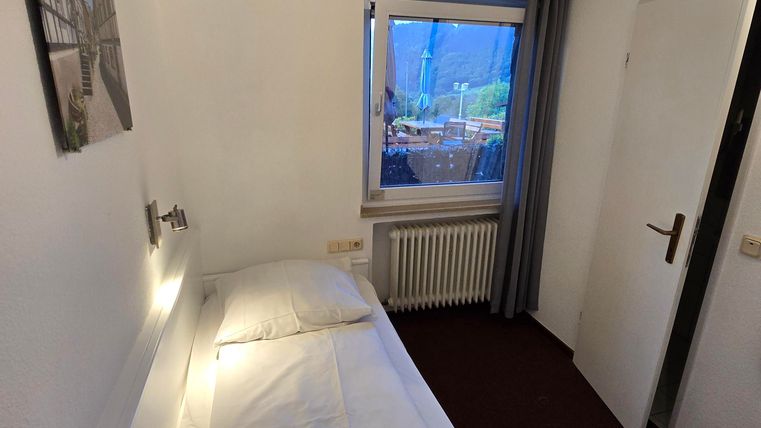 A simple single room with a bed and a window. The walls are light, and there is a radiator as well as a wardrobe.