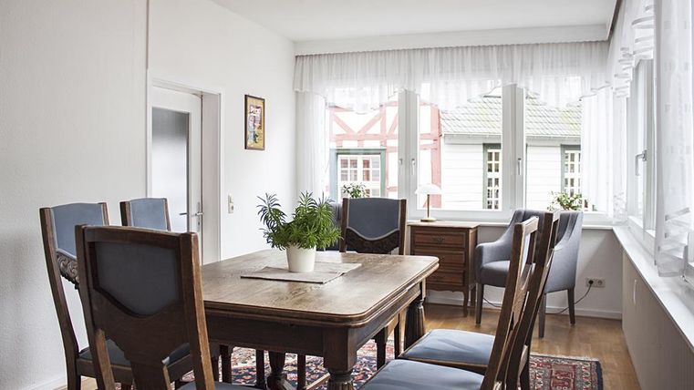 Een lichte eetkamer met een houten tafel en stoelen. Grote ramen zorgen voor veel daglicht en een aangename sfeer.