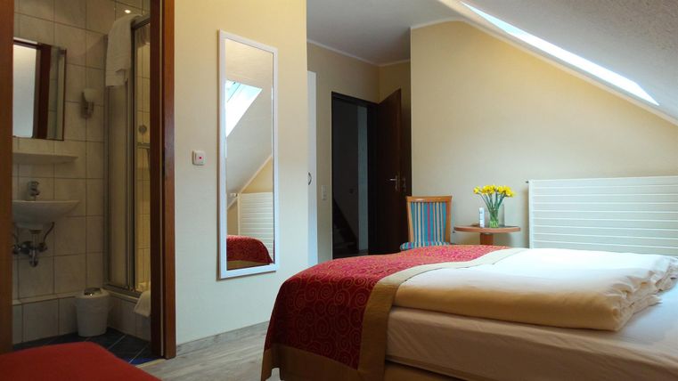 Een gezellige kamer met een tweepersoonsbed en een douche. Het zonlicht stroomt door het raam en zorgt voor een uitnodigende sfeer.