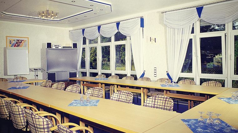 Een moderne vergaderruimte met een grote tafel en tal van stoelen. Grote ramen laten veel licht binnen en bieden uitzicht naar buiten.