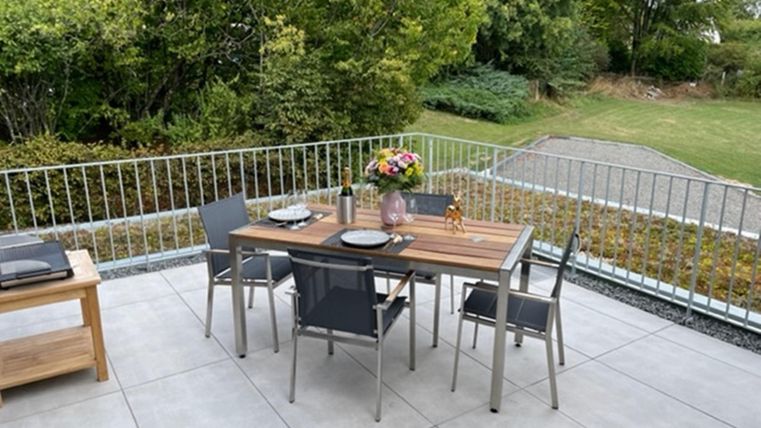 Een uitnodigend balkon met een elegante tafel en stoelen. Op de tafel staat een bloemenvaas en servies, omringd door groene vegetatie.