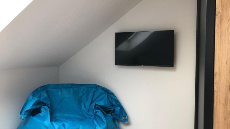 A cozy room with a blue bean bag and a wall-mounted television. The walls are bright, and the floor is wooden.