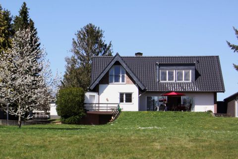 A modern house with a black roof and a balcony.
Surrounded by green grass and trees.