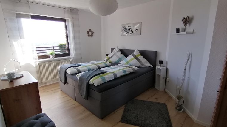 A cozy bedroom with a large double bed and colorful pillows. The room is bright and cheerful, with a window that provides natural light.