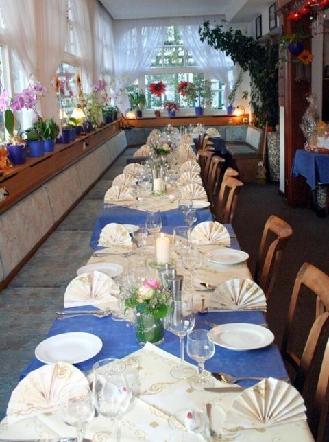 Ein festlich gedeckter Tisch mit blauen Tischdecken und dekorativen Servietten. Der Raum ist hell mit Pflanzen und Blumen dekoriert.