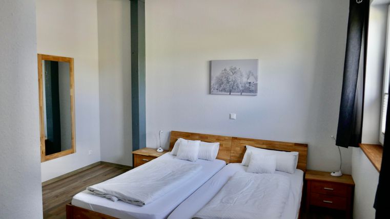 A bright bedroom with two single beds and a wooden wardrobe. A picture hangs on the wall, and a large mirror is also visible.