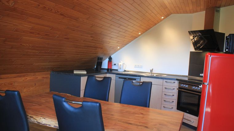 A modern kitchen with a wooden ceiling and bright walls. The room features a wooden dining table and modern kitchen appliances.