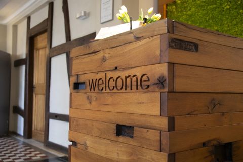 A reception desk made of wood with the inscription "welcome". In the background, there is a vibrant plant wall.