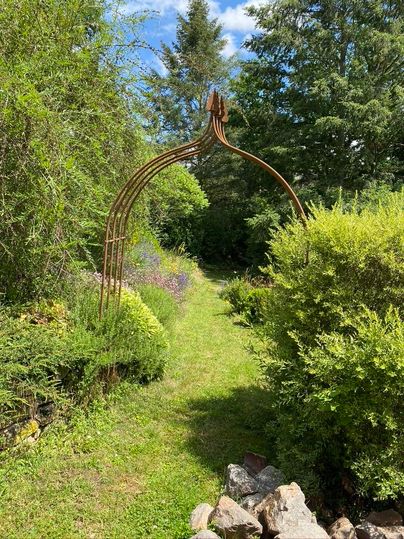 Een smaakvolle tuinpad met een rustieke metalen poort. Omringd door weelderig groen en kleurrijke bloemen leidt het pad de natuur in.
