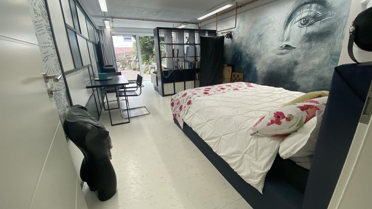 Een moderne kamer met een groot bed en beddengoed met bloemenpatroon. Aan de muur hangt een indrukwekkende muurschildering, en er is een kleine werkplek met een tafel en stoel.