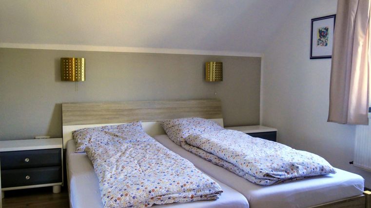 A cozy bedroom with two separate beds and colorful bedspreads. Two lamps are hanging on the wall, and a nightstand is next to it.