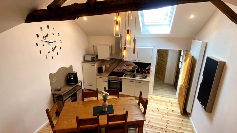 Een moderne keuken met een houten tafel en stoelen. Het plafond heeft zichtbare balken en grote ramen zorgen voor veel licht.