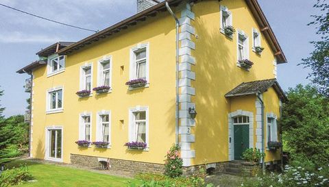 A beautiful yellow house with white windows and blue flower boxes. The garden is well-maintained and surrounded by greenery.
