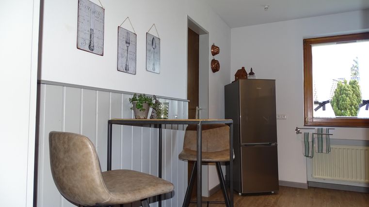 Een moderne keuken met een hoge tafel en twee stoelen. De muren zijn versierd met schilderijen en er is een raam met uitzicht op buiten.