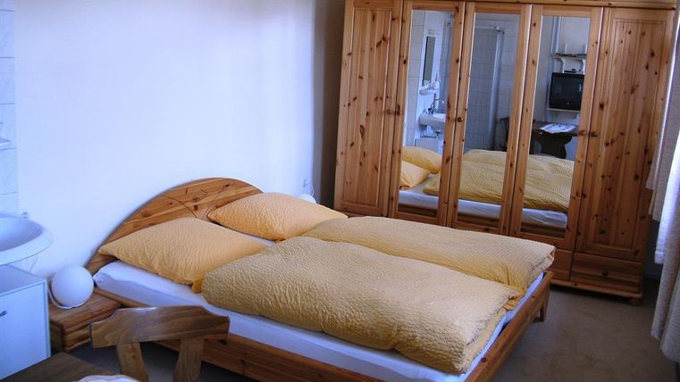 A cozy bedroom with a double bed and wooden furniture. The room has a bright atmosphere and a large wardrobe with mirrors.
