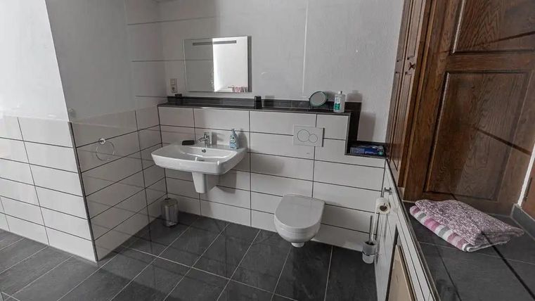 Ein modernes Badezimmer mit weißen Fliesen und dunklem Boden. Es gibt ein Waschbecken, eine Toilette und einen Spiegel.