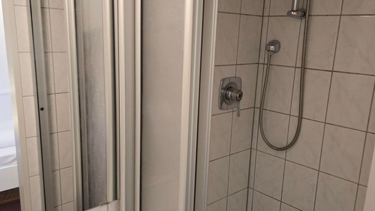 A modern shower with glass partition and bright tiles. Next to the shower is a washbasin.