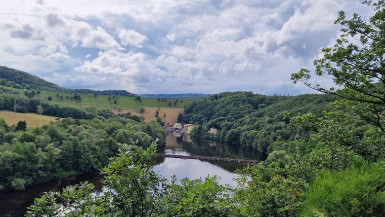 A picturesque landscape with a river and lush greenery. The sky is cloudy, but nature looks inviting.