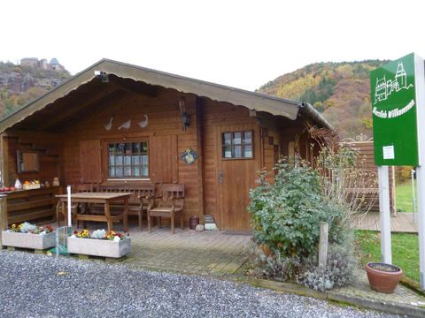 Een gezellig houten huis met een terras en bloeiende planten. De omgeving wordt gekenmerkt door zachte heuvels en herfstkleuren.
