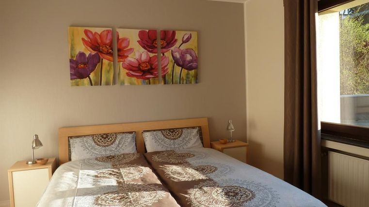 A cozy bedroom with a double bed and colorful flower pictures on the wall. The windows let in plenty of daylight and create a bright atmosphere.