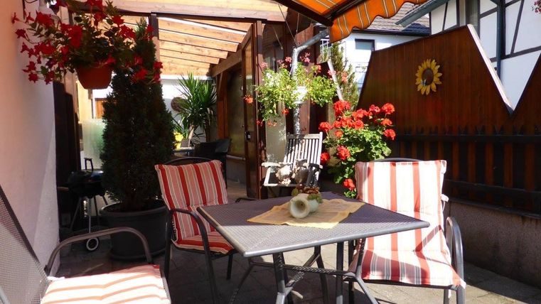 Een gezellige buitenruimte met gestreepte stoelen en een tafel. Kleurrijke bloemen en planten zorgen voor een uitnodigende sfeer.