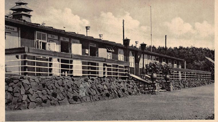 A historic building with multiple windows and a porch.
Surrounded by well-maintained grounds and trees in the background.