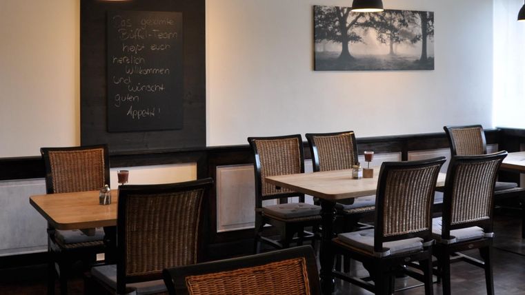 Een gezellig restaurant met houten stoelen en tafels. Aan de muur hangt een bord met tekst en een afbeelding van bomen.