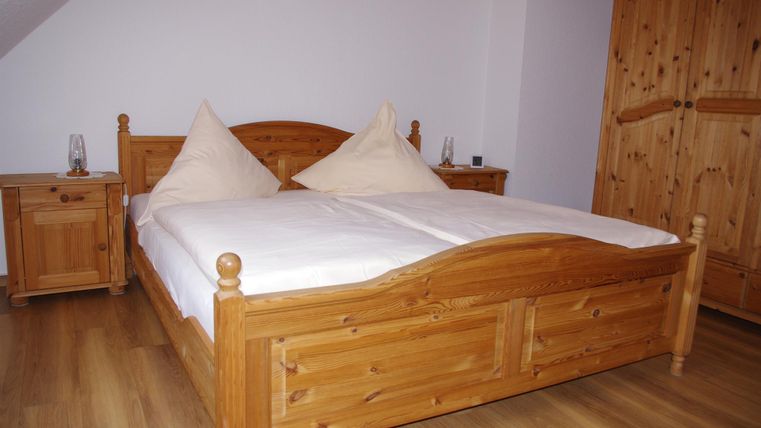 A cozy bedroom with a large wooden double bed. Next to the bed are nightstands and a wooden wardrobe.