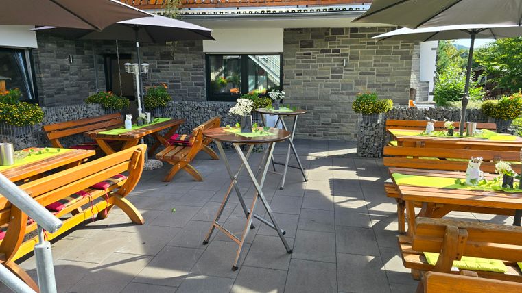 An inviting outdoor area with wooden tables and sun umbrellas. Plants and decorations create a cozy atmosphere.