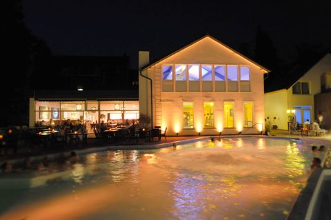 Ein schöner Pool bei Nacht, umgeben von beleuchteten Gebäuden. Sanfte Lichter reflektieren sich auf dem Wasser.