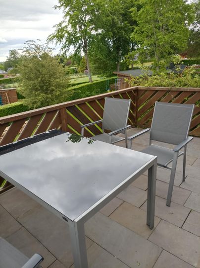Ein gemütlicher Balkon mit einem modernen Tisch und Stühlen. Im Hintergrund sind grüne Bäume und eine gepflegte Gartenlandschaft sichtbar.