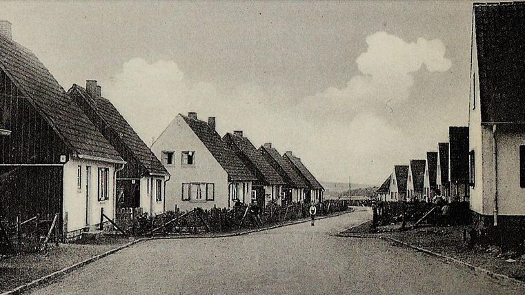 Eine ruhige Straße mit einfachen, einheitlichen Häusern. Der Himmel ist bewölkt und die Umgebung wirkt friedlich.