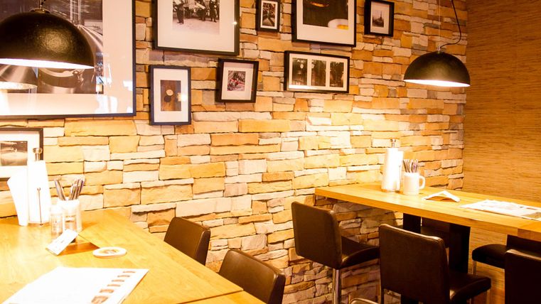 A cozy café with wooden tables and a stone facade. Black-and-white photos hang on the walls, and the lighting is warm and inviting.