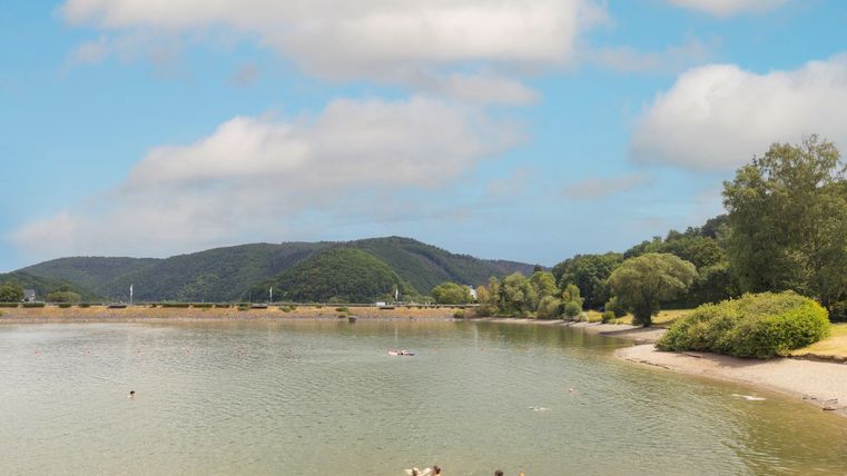 Eine ruhige Bucht mit klaren Wasser und sanften Wellen. Im Hintergrund sind Hügel und grüne Bäume zu sehen.