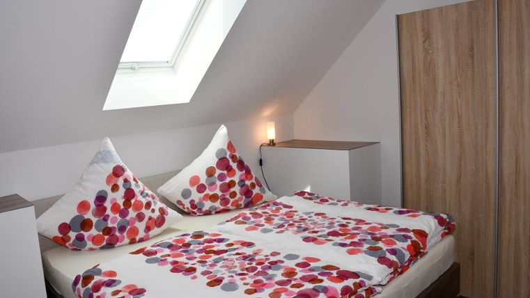 Een gezellige slaapkamer met een tweepersoonsbed en kleurrijke kussen. De kamer heeft een dakraam en moderne meubels van hout.