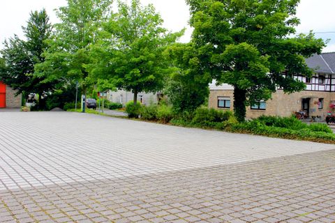 Een lege plaats met een betegelde vloer en enkele bomen. Op de achtergrond zijn gebouwen te zien.