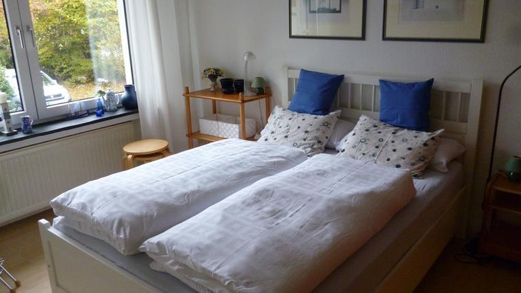 Een gezellig slaapkamer met een wit bed en blauwe kussens. Grote ramen laten veel daglicht binnen.